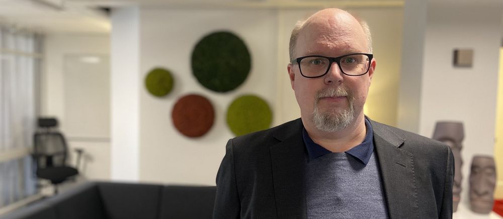 Thomas Gustafsson (S) står i en kontorsmiljö och tittar in i kameran.