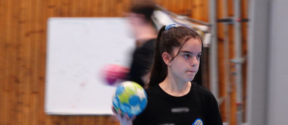 Handbollsspelare med boll i handen under en inomhusträning. Trävägg och whiteboard i bakgrunden.