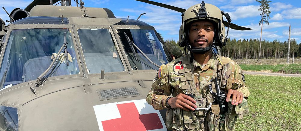 En ung man står i militära kläder framför en Blackhawk helikopter.