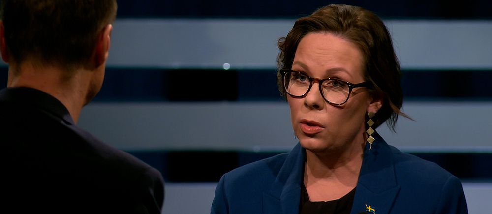 Två personer står mitt emot varandra i en tv-studio under en intervju eller debatt.