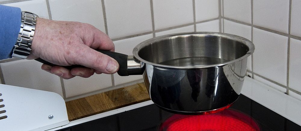 kastrull fylld med vatten. kastrullen hålls strax ovanför en röd upphettad spisplatta.