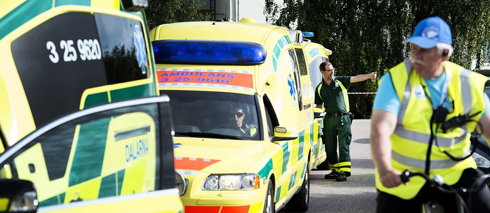 Två ambulanser står parkerade på en asfalterad väg. En man med reflexväst cyklar i förgrunden.
