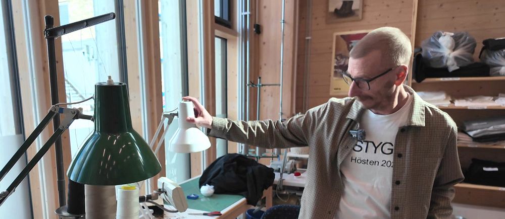 David Åkerlund visar en syateljé med symaskin och arbetsbord i bakgrund.