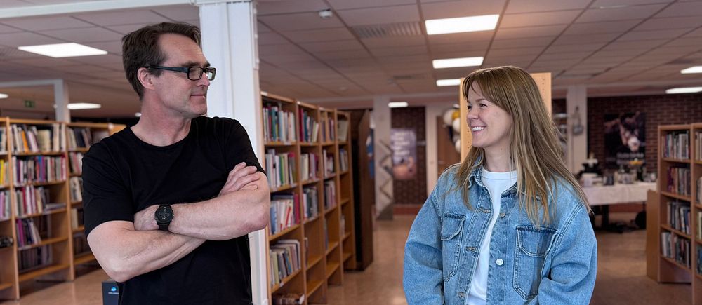 Två personer samtalar framför bokhyllor i ett bibliotek.