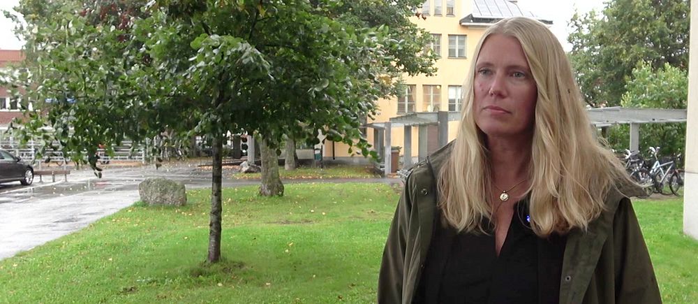 En kvinna står på en gräsmatta framför ett träd