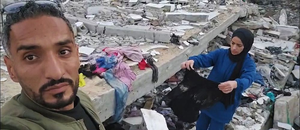 Kvinna granskar kläder vid ruiner i Gaza.