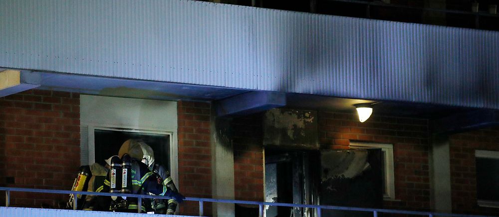Brandman i rökdykarutrustning vid en sotig och brandskadad lägenhetsbalkong.