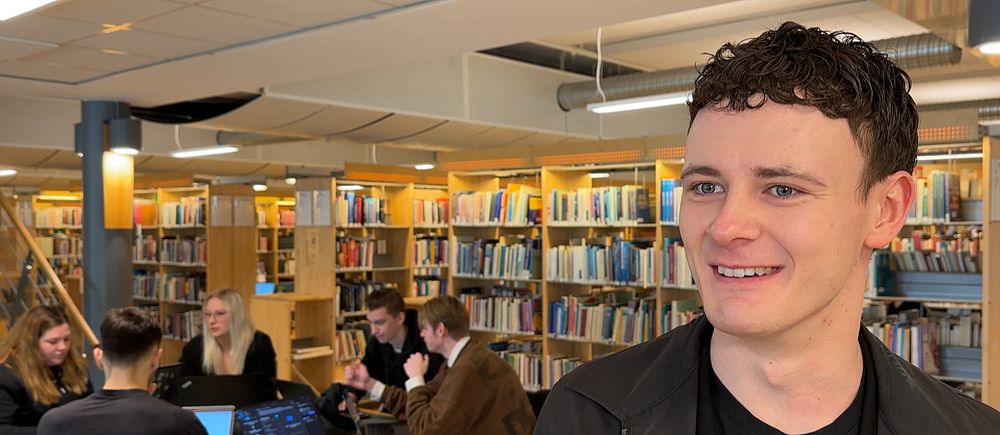 Studenter arbetar vid bord i ett bibliotek, omgivna av bokhyllor.