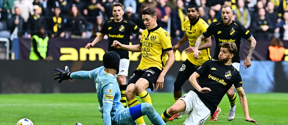 Fotbollsmålvakt räddar ett skott nära mål under en allsvensk match inför fullsatt läktare.