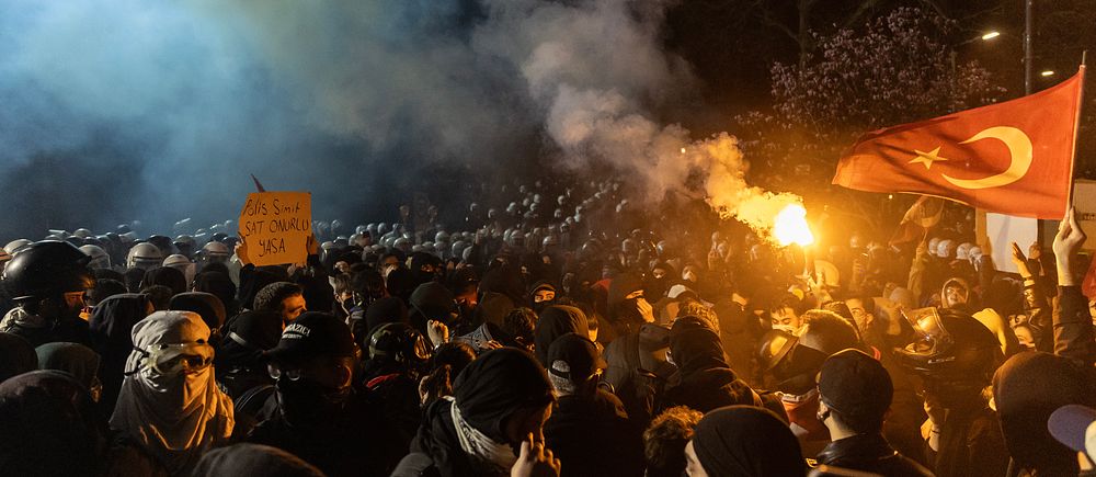 Folkmassa protesterar med turkisk flagga och facklor, rök fyller natthimlen.