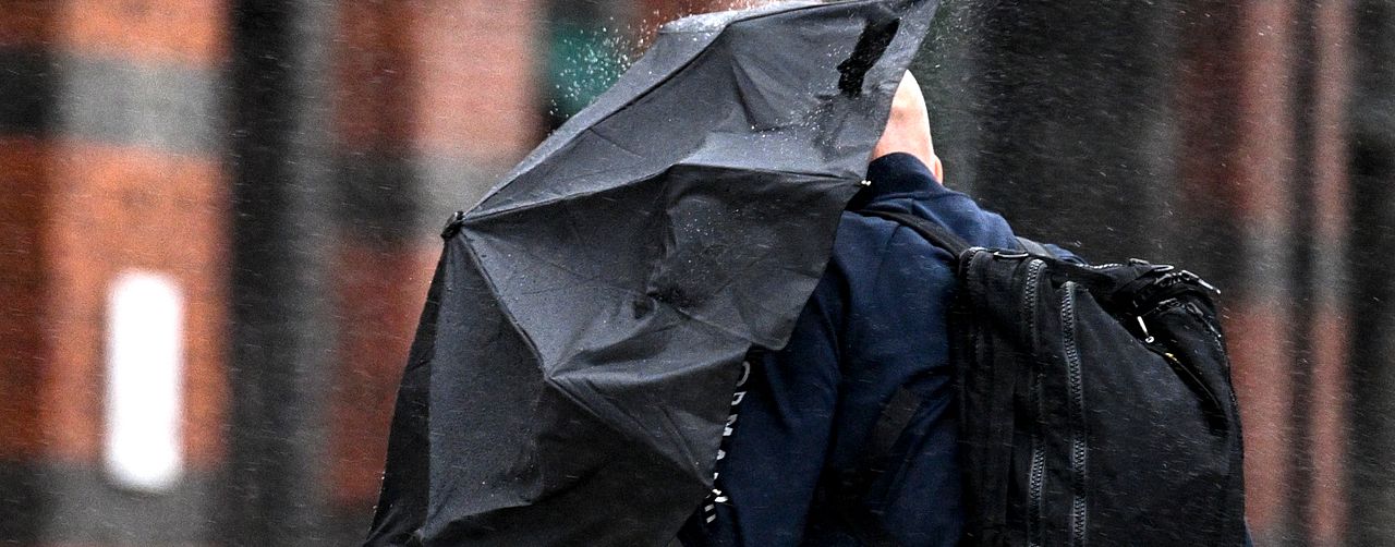 En man med ett svart paraply i spöregn.