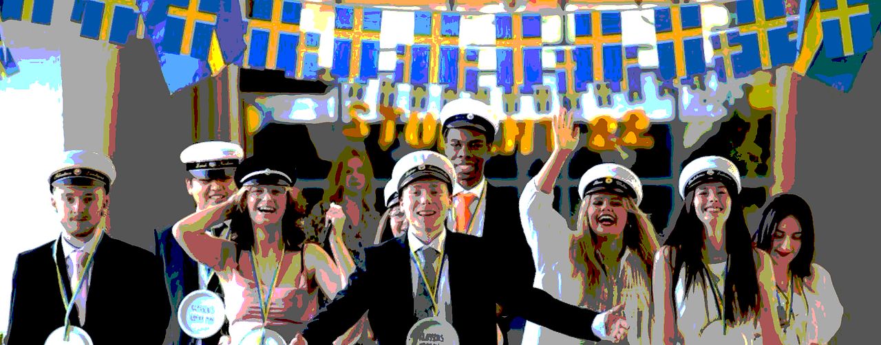 Studenter med studentmössor under svenska flaggor som hänger över dem.