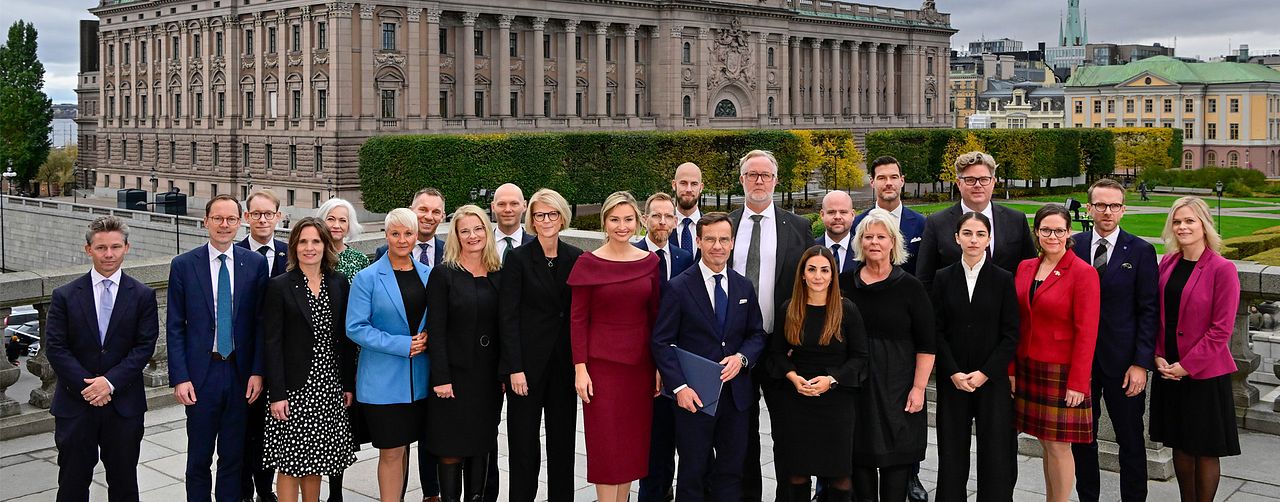 Sveriges ministrar uppställda med riksdagshuset i bakgrunden.