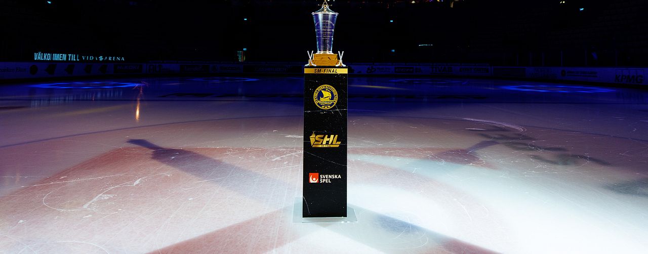 SHL-pokalen i centrum av en isrink, upplyst av strålkastare, omgiven av läktare i bakgrunden.