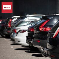 Flera parkerade bilar i rad, inklusive vita, svarta och grå fordon, på en parkeringsplats i dagsljus. Bakgrunden är otydlig.