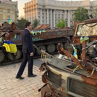 Tvådelad bild. Till vänster Sveriges bistånds- och utrikeshandelsminister Benjamin Dousa som promenerar förbi stridsvagnar med Ukrainska flaggor på. Till höger en bild från ett skyddsrum i Ukraina.