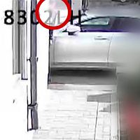 En suddig bild från en övervakningskamera, en person ses titta fram bakom ett hörn.