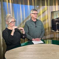 Gästen Lars Arrhenius står i en studio med programledaren Magnus Bergevin och en teckenspråkstolk.