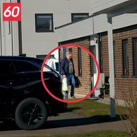 En man, Nils Thuresson, i blå jacka och kasse utanför ett tegelhus, markerad med röd cirkel.