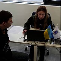 Rekryteringskontor för den ukrainska armén med kvinna och man sittandes vid bord, till höger skylt i gatumiljö