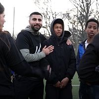 Ungdomar som står i klunga på en fotbollsplan i Skärholmen. De tycker att det är viktigt att verksamheten fortsätter trots att de håller till bara ett stenkast från där Mikael sköts till döds.