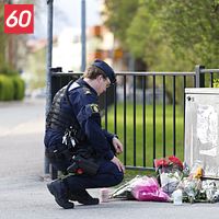 Två poliser vid ett minnesmärke med blommor på trottoar nära ett staket.