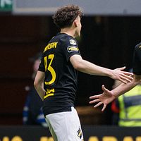 Två AIK-spelare på fotbollsplan med sträckta händer, publik och vakter i bakgrunden.