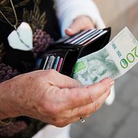 Äldre kvinna tar pengar ur en plånbok