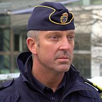 Henrik Dahlström i uniform vid en gata, med polisbilar i bakgrunden.
