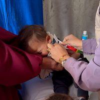 Barn vaccineras av vårdpersonal, hålls försiktigt av en vuxen.
