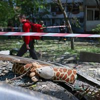 En gosedjursgiraff ligger bland bråte, räddningsarbetare går förbi bakom avspärrningsband.