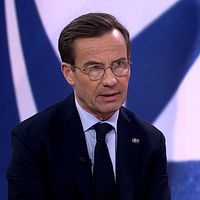 Person i kostym med NATO-logotyp som bakgrund.