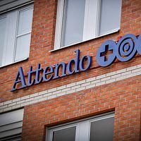 Skylt med Attendos logotyp på brun tegelvägg.