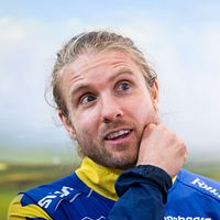 Person i gul-blå sporttröja står utomhus med landskap i bakgrunden.