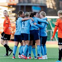 Fotbollslag i blåa tröjor firar på planen, motståndare i orangea tröjor syns i bakgrunden.