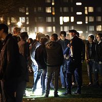 En polis står med ficklampa vid en stor grupp ungdomar på Hoppbacken i Enskede under valborgsnatten.