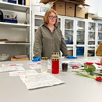 Laboratoriebord med ljus, papper och rosor, person i bakgrunden bakom bordet.