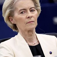 En kvinna i ljus kavaj sitter i vad som ser ut att vara en formell miljö.