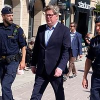 Justitieminister Gunnar Strömmer (M) går längs Storgatan i Sundsvall. På vår sin sida om honom går två uniformklädda poliser.