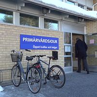 entrén till primärvårdsjouren i Umeå, en gul tegelbyggnad, en blå skylt med öppettider, en man som går in genom dörren