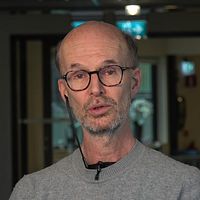 Person står i ett kontorsliknande miljö med glaspartier och suddig text på väggen.