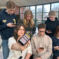 Ungdomar använder mobiltelefoner i en skolmiljö, SVT:s reporter visar skärmen mot kameran.