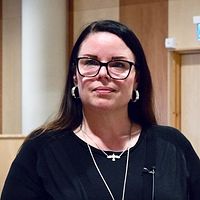 Stina Michelson (S) står i en kommunsal, mikrofon och bänkar syns i bakgrunden.