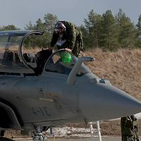 Pilot kliver ur ett militärflygplan på en flygbas, personal står bredvid.