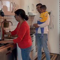 Sumayia Rahman vid diskhon i ett kök, Ezazul Haque står bredvid och håller i deras barn Ethan Haque i famenen.