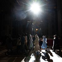 En grupp personer går genom ett mörkt kyrkorum med ett starkt ljussken ovanifrån.