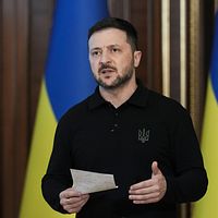 Person håller tal framför ukrainska flaggor och håller ett papper i handen.