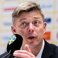 Jon Dahl Tomasson på en presskonferens med en mikrofon framför sig.