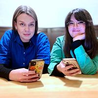 Två kvinnor sitter vid ett bord med sina telefoner.