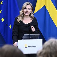 Ebba Busch vid talarpodium med Sveriges och EU:s flaggor i bakgrunden.
